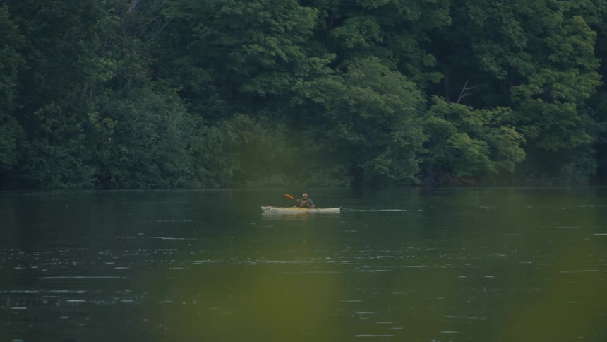A person is kayaking on a calm body of water using a doublebladed paddle to propel a yellow kayak forward
