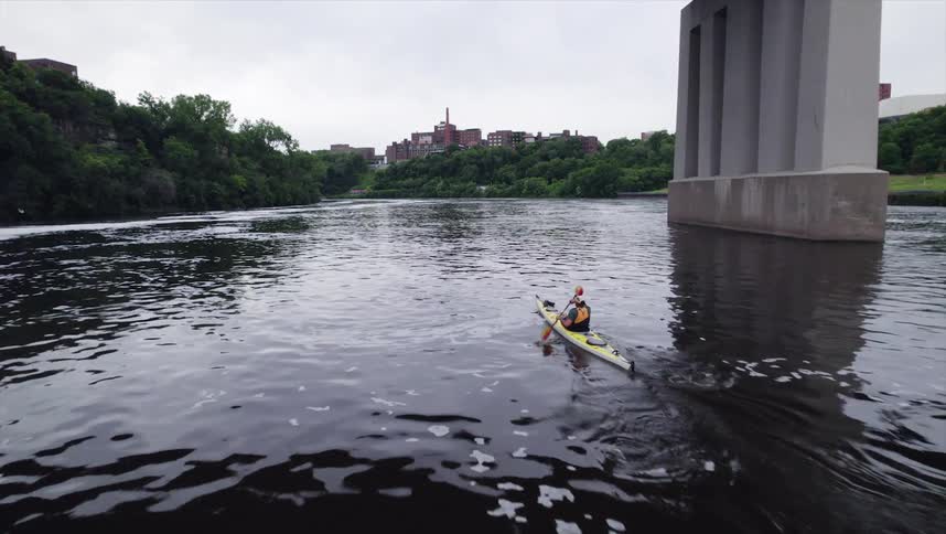 Person performing canoeing on a river below a bridge