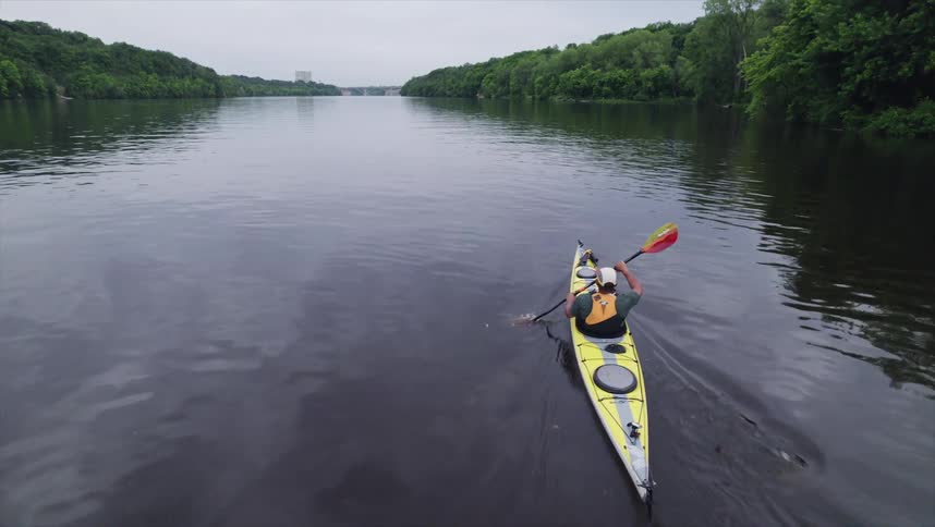 A person is kayaking on a calm river using a doublebladed paddle to propel a yellow kayak forward