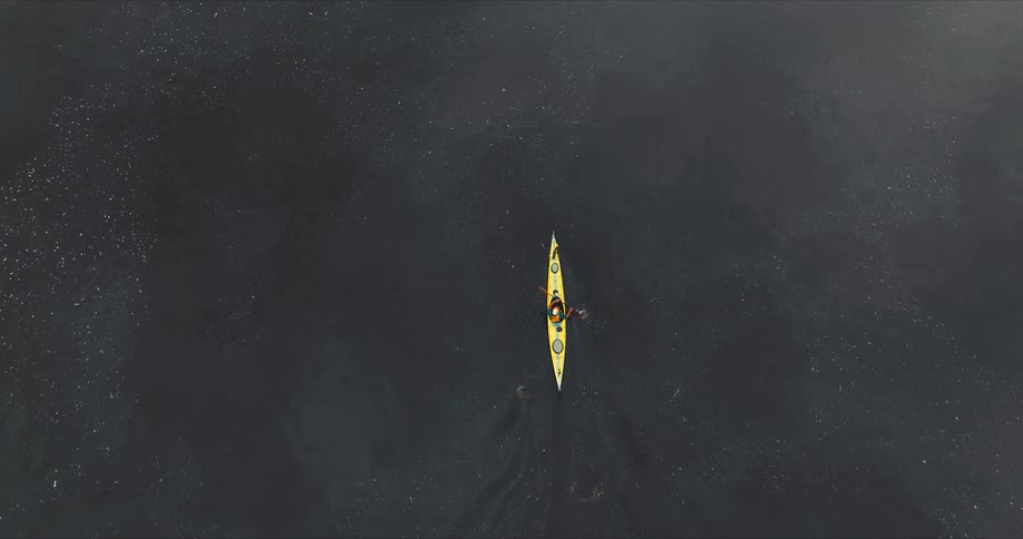 A person is paddling a yellow kayak on a dark calm body of water viewed from above