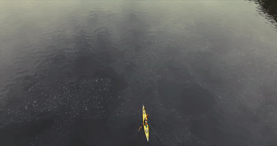 A person is kayaking alone in a yellow kayak on a vast calm body of water