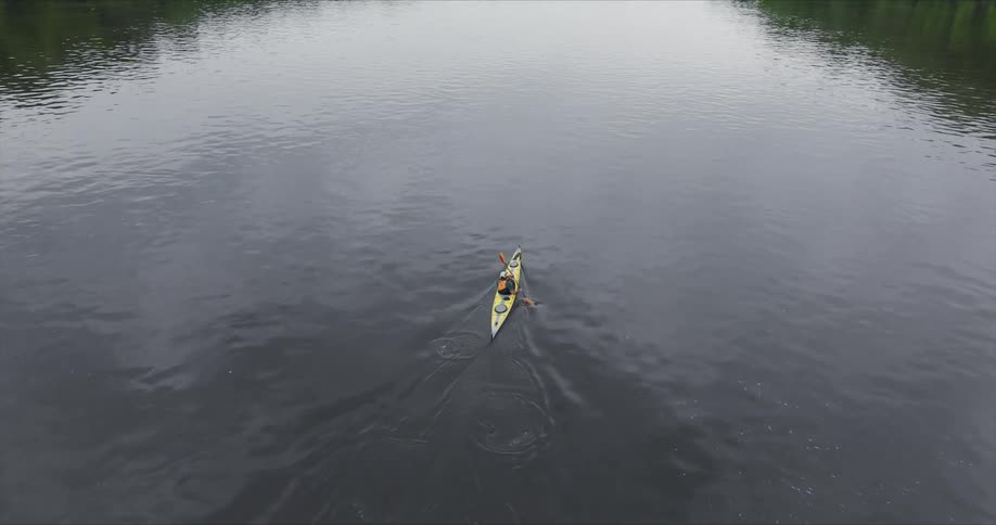 The kayaker paddles with a steady rhythm their movements creating ripples on the otherwise still surface of the lake