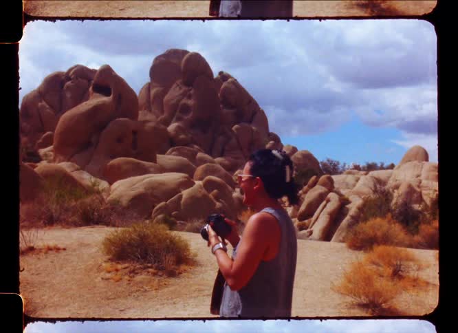 A person taking pictures in a desert landscape with large rock formations under a partly cloudy sky