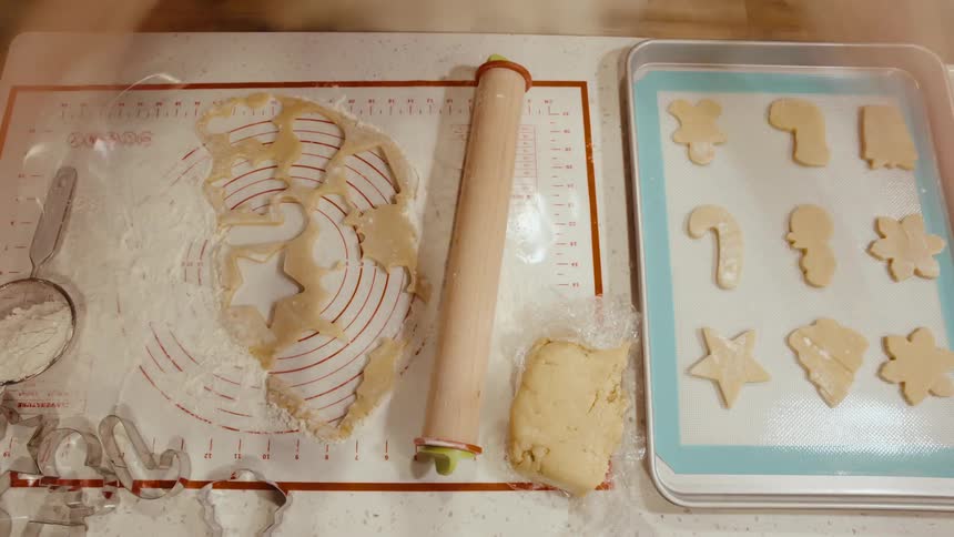 Two people work together in a kitchen one rolling out dough and the other cutting out cookie shapes