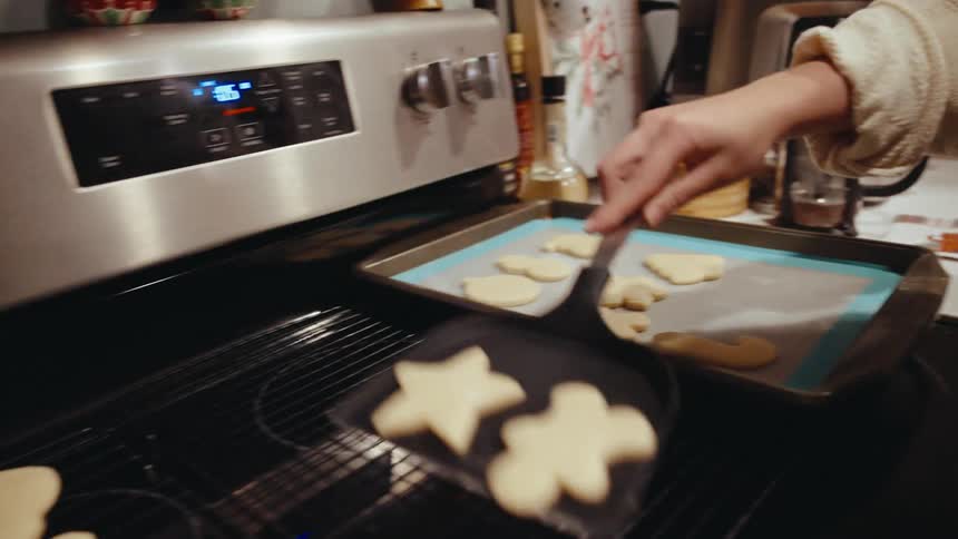 A woman removes a baking sheet of freshly baked christmas cookies from the oven