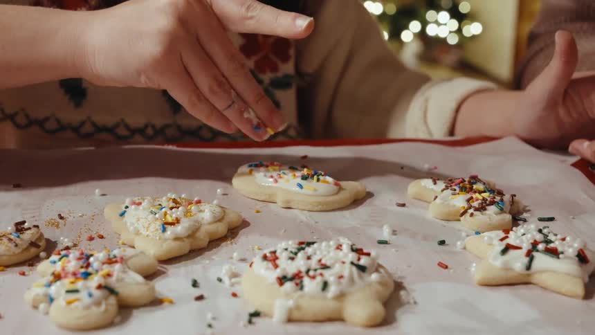 A woman puts sprinkles on the cookies