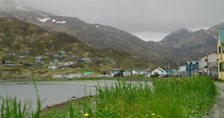 A small coastal town with colorful houses is nestled at the foot of a mountain range