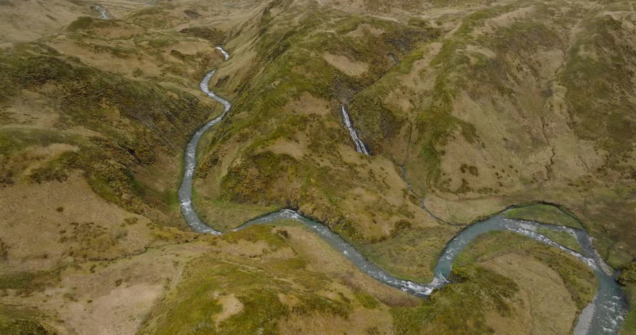 A river snakes its way through a rugged landscape carving a path through rolling hills and cascading waterfalls
