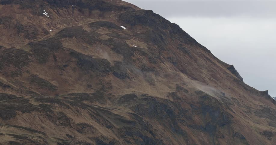 A rugged brown mountain landscape with patches of snow and a thin layer of mist partially covers the slopes