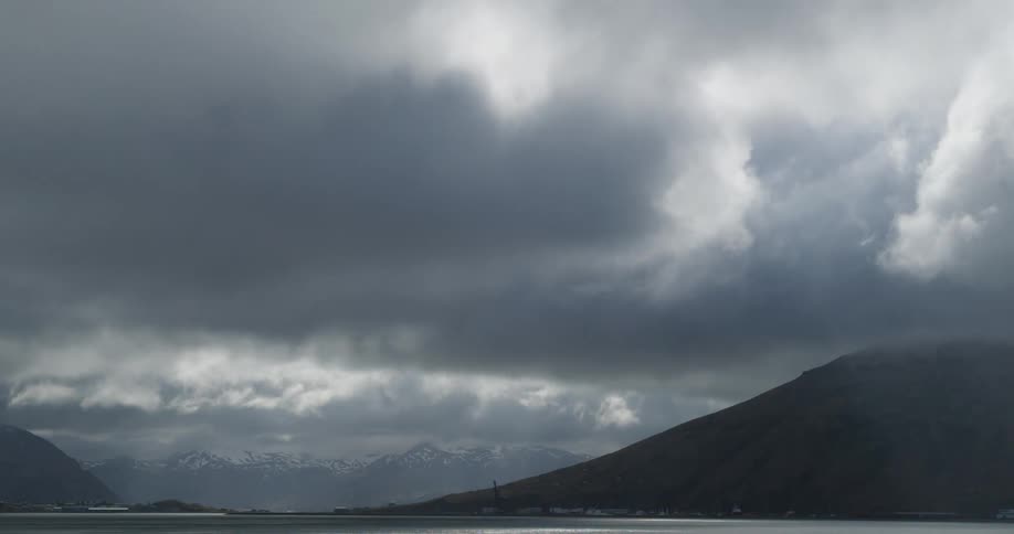 Grey clouds float over a lake and mountains