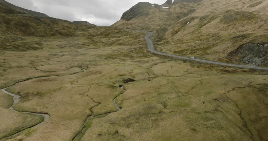 A lone car winds its way along a desolate road snaking through a barren landscape of brown hills and rocky terrain