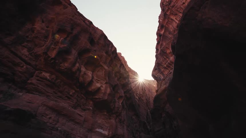 A shaft of sunlight pierces through a narrow chasm between towering sandstone cliffs casting a dramatic glow on the surrounding rock walls