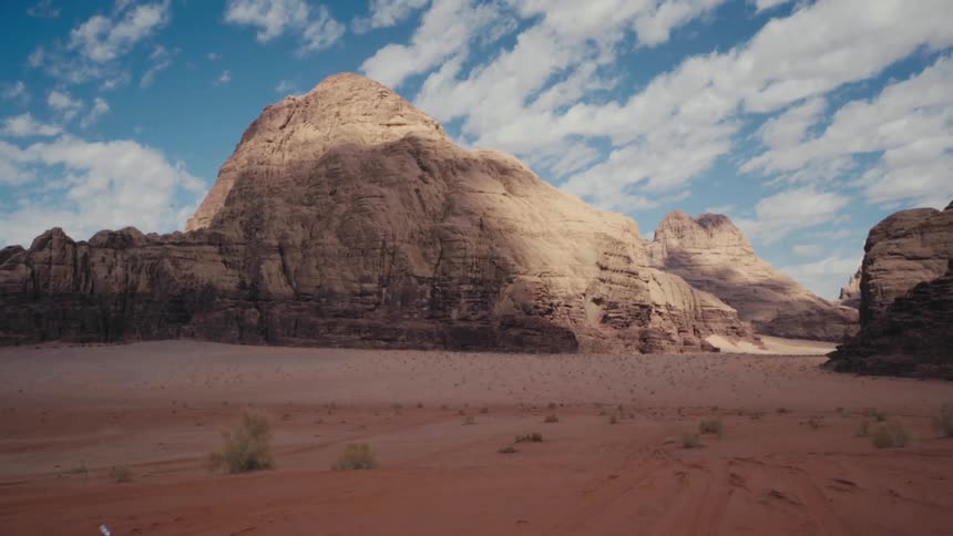 Towering sandstone cliffs rise dramatically from the desert floor under a vast blue sky
