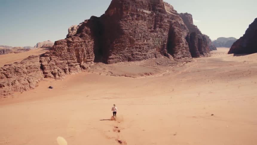 Woman running down a sandy desert hill with canyons in the background