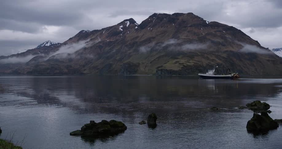 A fishing boat sails past a mountainous island shrouded in mist