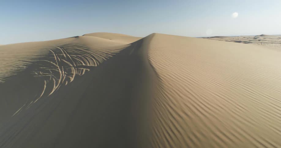 Aerial view of a series of tire tracks on sand dunes under a clear sky