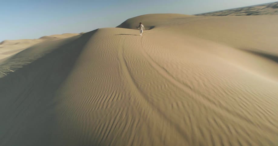 A lone figure running across a vast undulating desert landscape under a clear sky
