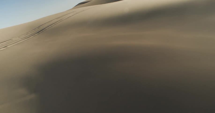 A vast sandy desert landscape with rolling dunes and tire tracks visible on the surface