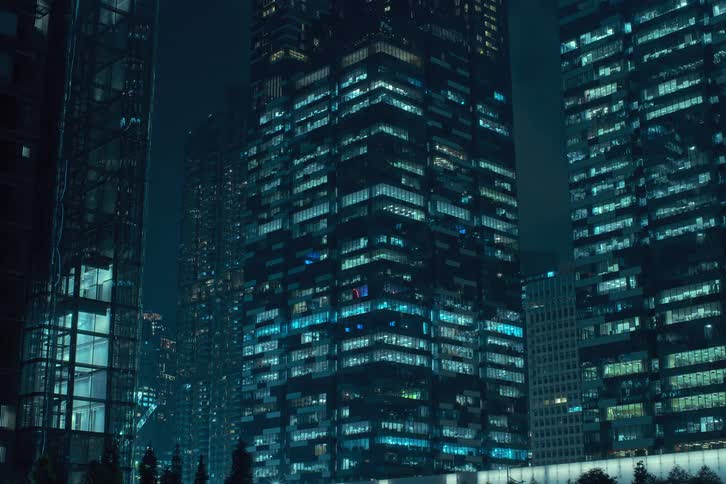 The exterior of modern high rise buildings at night with illuminated windows turning on