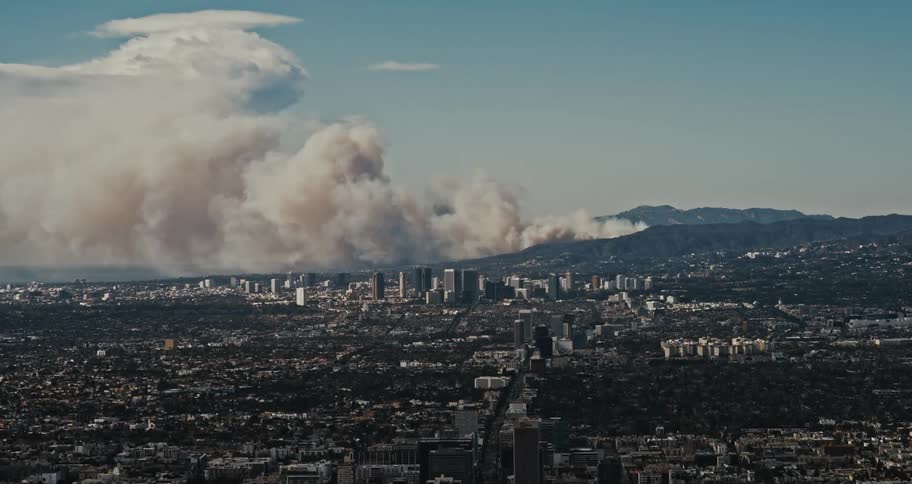 Panoramic view of a city with skyscrapers in the background while a large column of smoke rises from the mountains