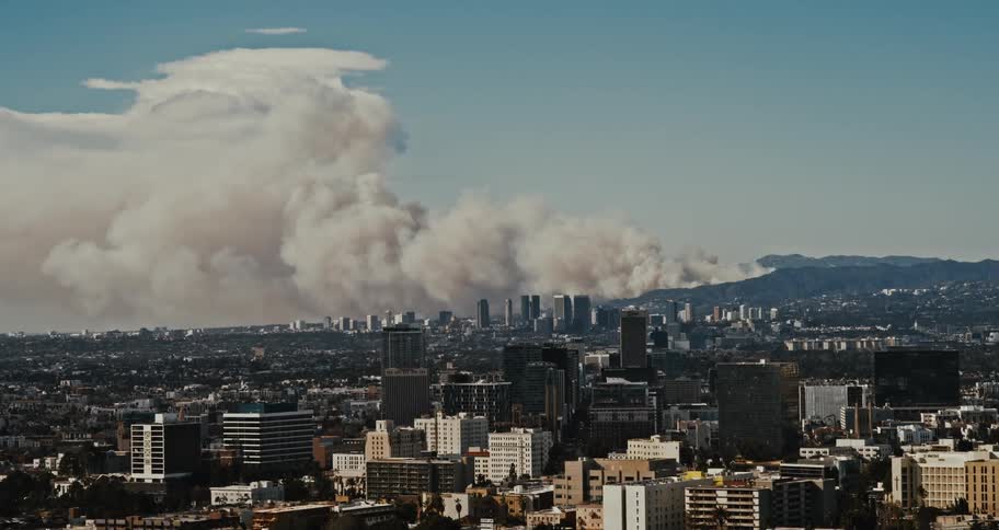 Smoke rises from fires burning near a large sprawling city during the daytime