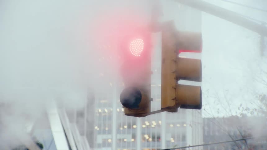 Smoke coming out of a red chimney in the middle of an urban street next to a traffic light
