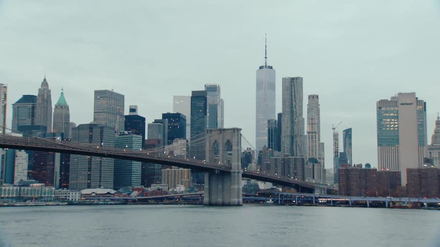 The brooklyn bridge with its distinctive suspension cables and stone towers spans the east river connecting brooklyn and manhattan while the citys skyline of skyscrapers rises in the background