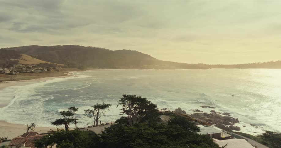 Aerial view ofa coastal town at sunset with a beach ocean waves and rolling hills in the distance