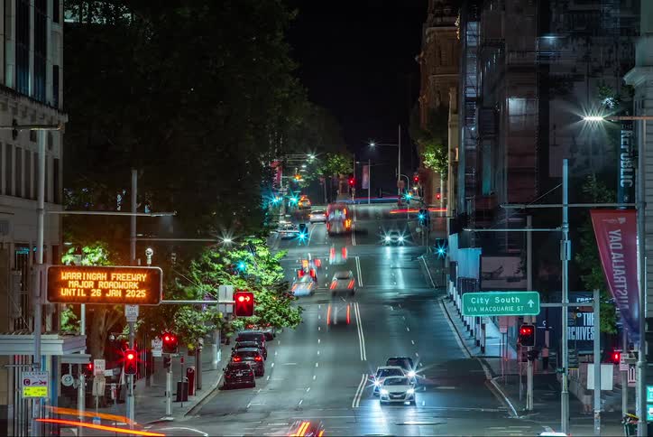 A street in a city at night with traffic moving along and streetlights casting a warm glow