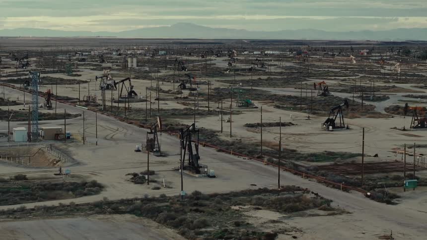 A vast oil field with numerous oil pumpjacks scattered across a barren landscape