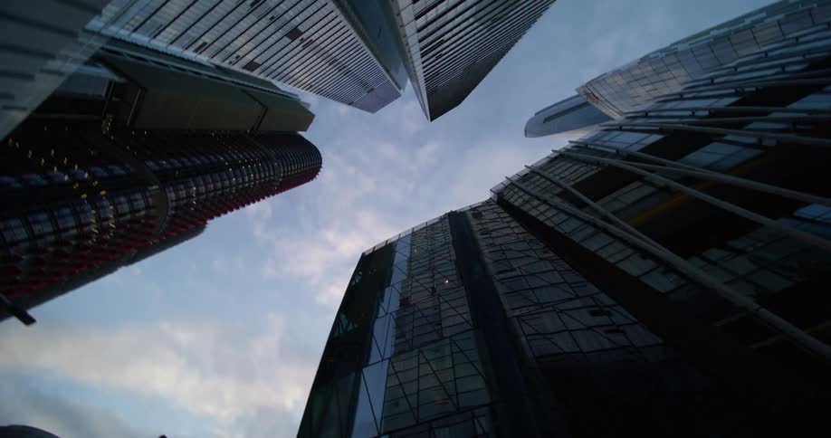 A lowangle perspective of a densely populated urban area showcasing a cluster of towering skyscrapers with reflective glass facades reaching upwards against a backdrop of a cloudy sky