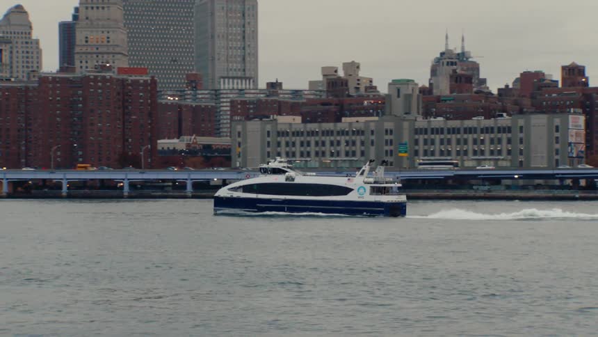 Panning left the camera tracks a ferry on the east river as it passes under the brooklyn bridge with the manhattan skyline in the background