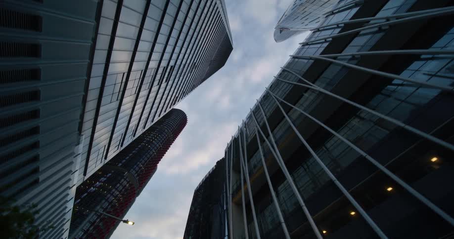 A lowangle view of a cityscape at dusk showcasing a cluster of towering skyscrapers with reflective glass facades reaching upwards against a backdrop of a twilight sky