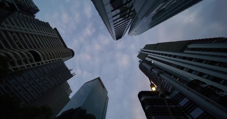 A view looking up at several tall skyscrapers from ground level with the buildings converging towards the center a backdrop of a cloudy sky