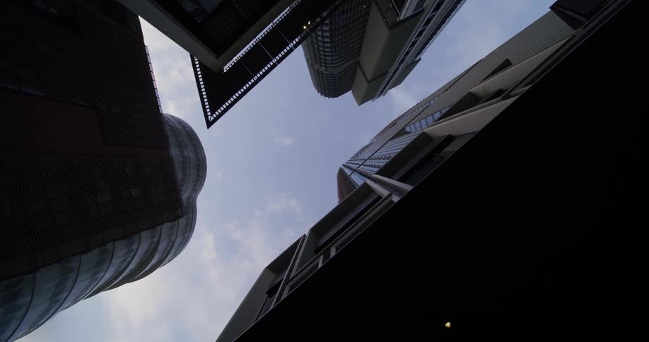 An upward view of modern buildings with varied architectural designs all converging towards a patch of sky in the center
