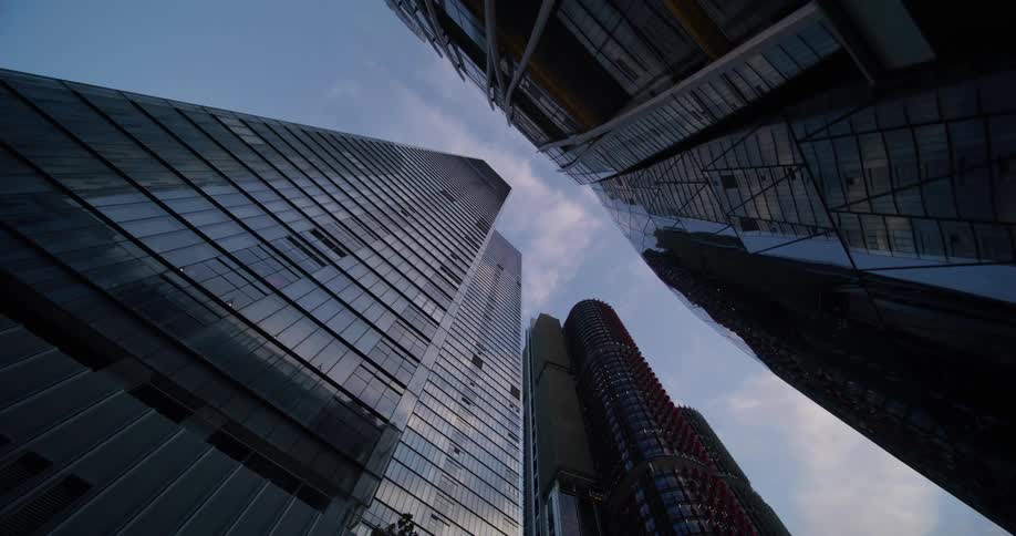 Several tall modern skyscrapers with glass facades reaching towards a blue sky with scattered clouds