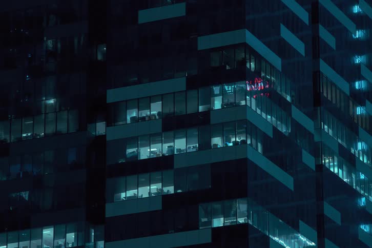 Nighttime view of a modern office building with numerous illuminated windows shutting down and turning off at the end of the day