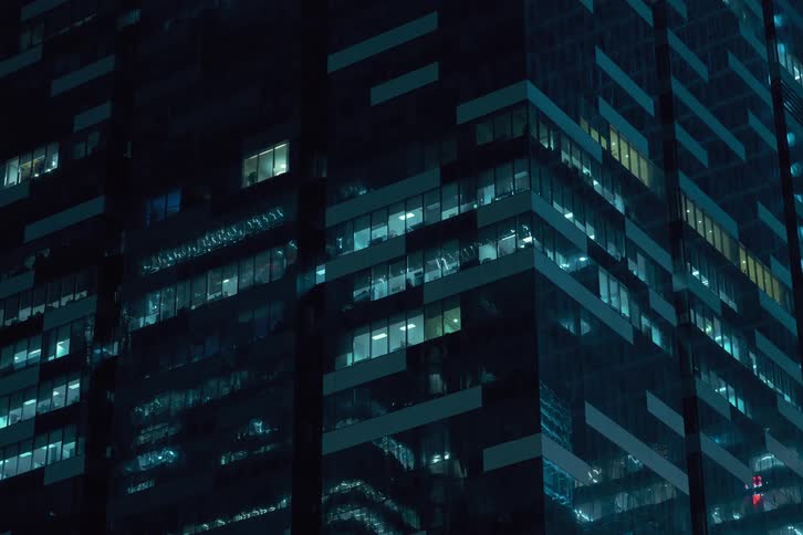 Nighttime view of a modern office building with numerous illuminated windows shutting down at the end of the day as they turn off together