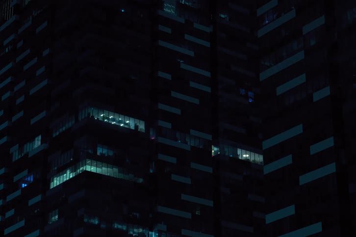 A nighttime view of a high rise building with many illuminated windows gradually darkening over time creating a dynamic contrast between light and shadow