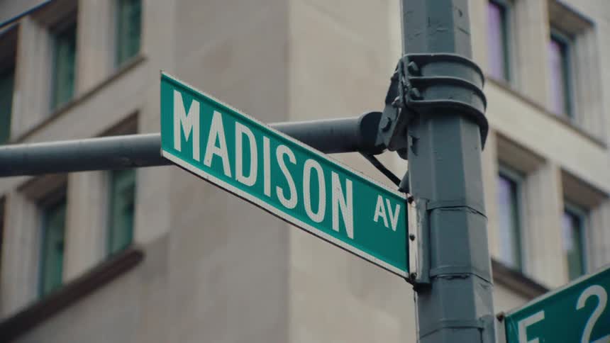The intersection of madison avenue and east 24th street with street signs mounted on a pole in front of a multistory building with numerous windows