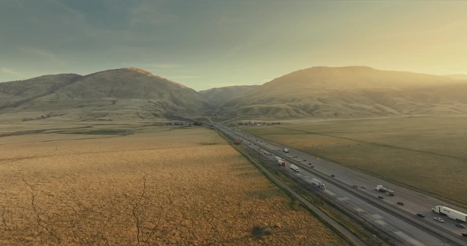 Aerial view of a highway with vehicle traffic and surrounded by green fields and mountains in the background