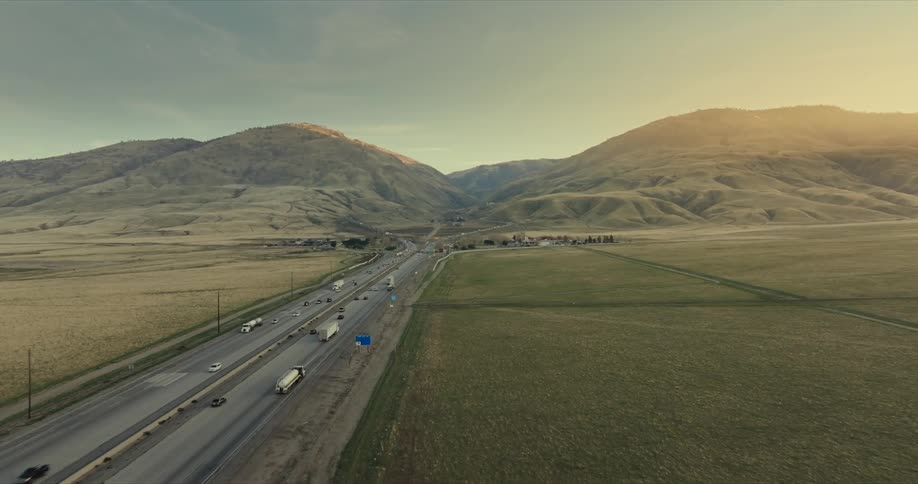 A highway running through a vast open landscape with rolling hills in the background under a clear sky with a warm golden light