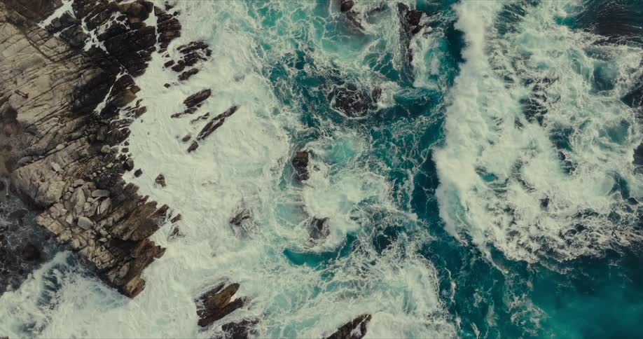 Aerial view of a turbulent ocean crashing against rocky cliffs