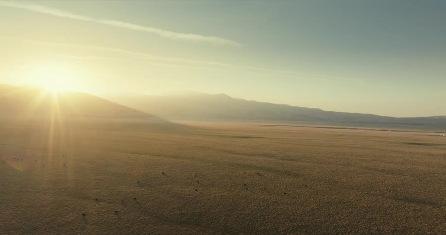 A vast dry landscape with a mountain range in the distance bathed in the warm glow of the setting sun