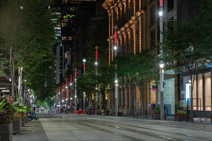 Trollies drive down the block as people walk on the sidewalk at night