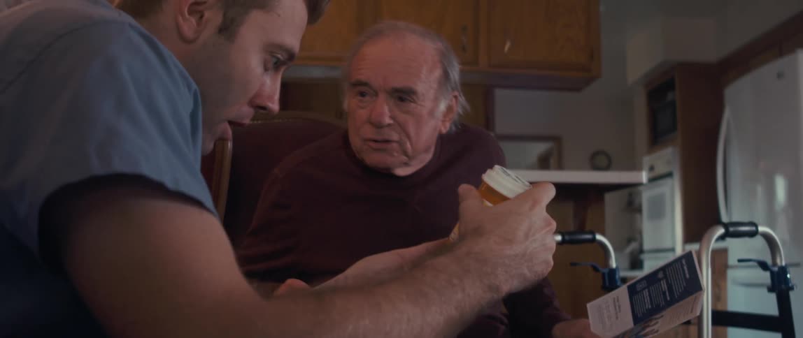 Nurse holding a bottle of medicine and talking to an elderly man next to him