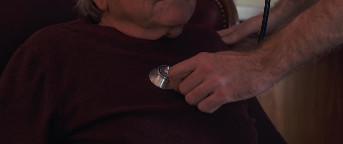 A male nurse cares for an elderly man in a cozy woodpaneled room at home