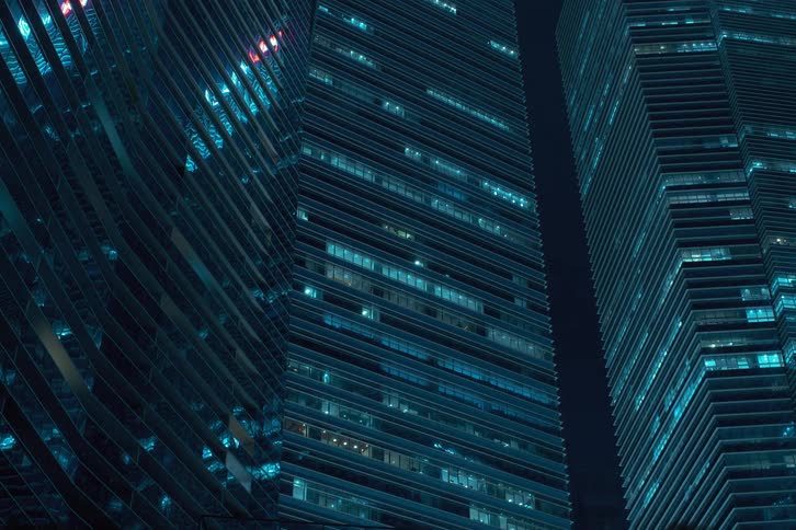 Nighttime view of modern office buildings with numerous illuminated windows shutting down and turning off at the end of the day