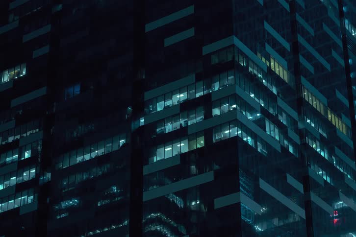 A towering skyscraper at night its glass facade reflecting the city lights and casting a mesmerizing glow