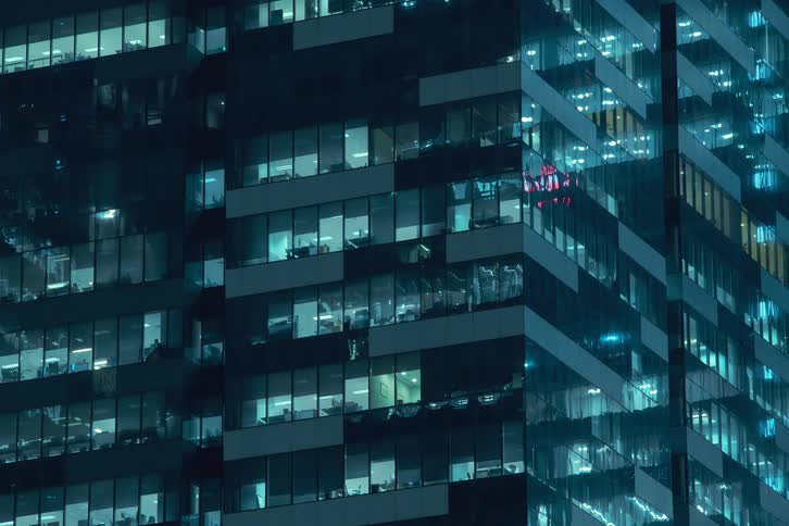 The facade of a modern highrise building at night with the windows flickering on and revealing the activity within